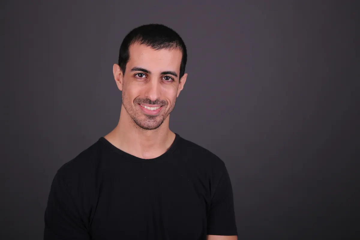 Homem de camiseta preta sorrindo em um retrato.